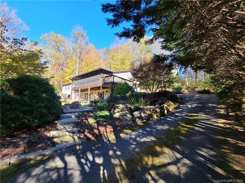 Paved driveway curving past stone-edged plantings and garden steps up to the house and its covered upper porch.