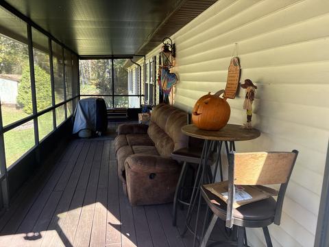 Screened porch with a sofa, a high-top table and stools along the house wall, with views out to the lawn and trees.