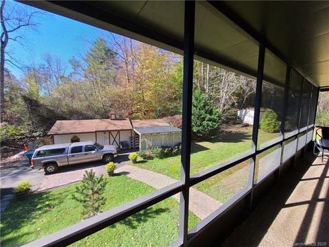 View from the screened porch over the lawn and brick walkway to a detached outbuilding, with a separate shed beyond.