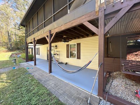 Covered lower patio under the screened porch, with heavy timber posts, a hammock, a porch swing and a paver walkway beside the lawn.