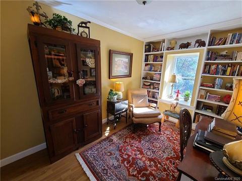 Room with wood floors, a red patterned rug, a glass-front cabinet and built-in bookshelves framing a window.
