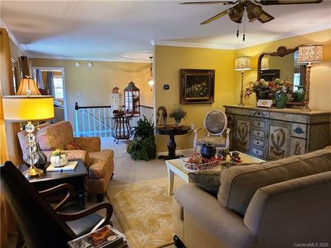 Living room with sofas, armchairs and a ceiling fan, opening toward the stair railing.