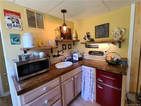 Lower-level mini kitchen with a wood-top counter, sink, microwave, open shelves and a small refrigerator.