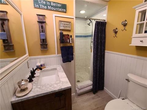 Bathroom with a marble-top vanity, beadboard wainscoting and a walk-in shower.